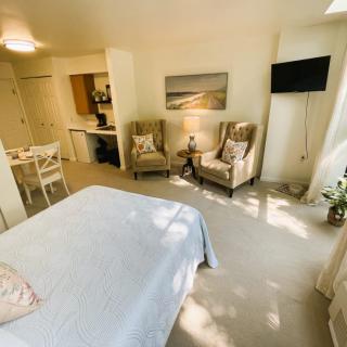 A cozy bedroom with a bed, armchairs, and a small TV, featuring soft lighting and elegant decor.