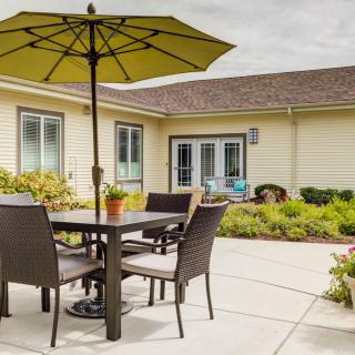 A cozy patio with a table and chairs set under a large umbrella, surrounded by a landscaped garden.