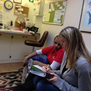 Two women are sitting and writing in an office space.