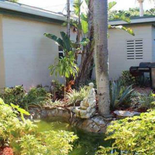 A lush tropical garden featuring a variety of plants, a palm tree, and a small statue.
