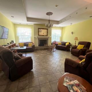 A cozy living room with sofas, a fireplace, and a television, featuring yellow walls and a chandelier.