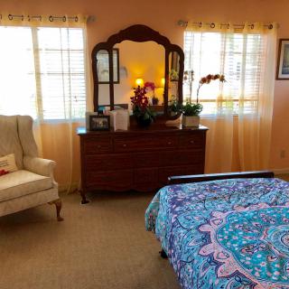 A cozy bedroom with a large wooden dresser and mirror, an armchair, and a bed adorned with a colorful bedspread.