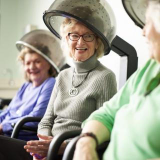 Elderly women enjoying conversation under hair dryers at a salon.