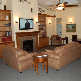 A cozy living room featuring a fireplace, brown sofas, bookshelves, and a TV mounted above the mantel.