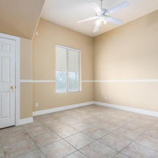 An empty room with beige walls, a tile floor, a window, and a ceiling fan.