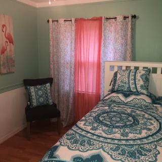 A cozy bedroom with turquoise bedding, decorated with colorful curtains and wall art.