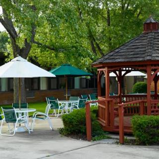 A serene outdoor setting featuring a wooden gazebo, patio furniture, and umbrellas surrounded by lush greenery.
