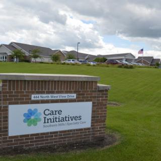 A sign for Care Initiatives in front of a healthcare facility, set against a backdrop of a cloudy sky.