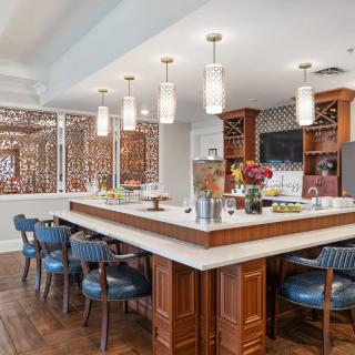 A modern kitchen and dining area featuring a large bar with pendant lighting, wooden cabinetry, and ample seating.