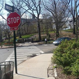 A view of a street intersection featuring a stop sign, vehicle, and surrounding greenery.