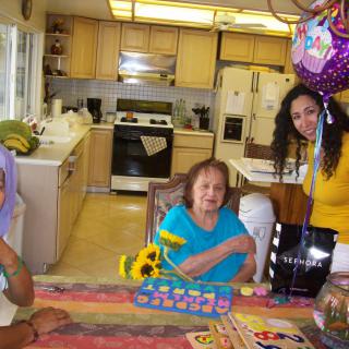 A family celebration in the kitchen with balloons and a cake on the table.