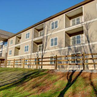 A residential apartment building with balconies and a wooden fence, set against a clear sky.