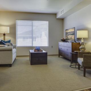 A cozy living room with a sofa, coffee table, and lamps, featuring a large window covered with blinds.