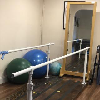 A physical therapy room equipped with parallel bars, exercise balls, and a mirror.