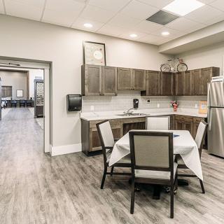 A modern kitchen with a small dining area featuring wood flooring, sleek cabinets, and a stainless steel refrigerator.