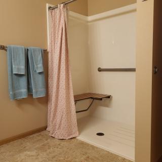 An accessible bathroom with a shower featuring a folding seat and grab bar.
