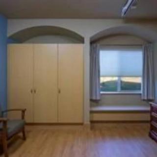 A room with a wardrobe, window seat, and wooden flooring.
