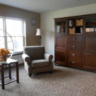 A cozy living room featuring an armchair, large bookshelf, and a window with natural light.