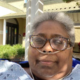 A woman wearing glasses smiles while enjoying the outdoors.