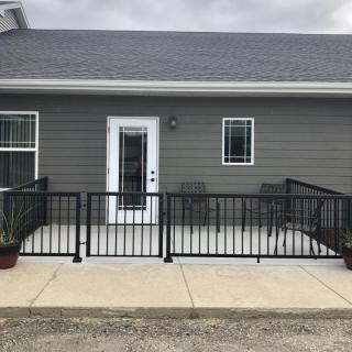 A small house with a porch featuring black railings, plants, and patio furniture.