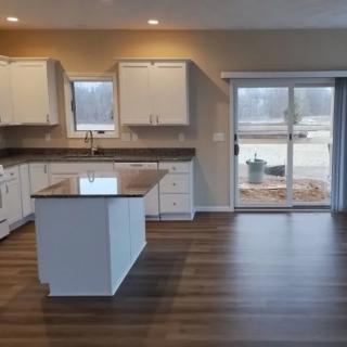 Modern kitchen with white cabinetry and a central island, featuring hardwood flooring and a large sliding glass door leading outside.