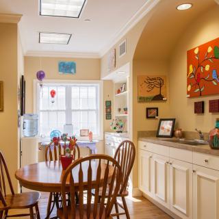 A cozy kitchen dining area with a table and chairs, adorned with colorful artwork and bathed in natural light.