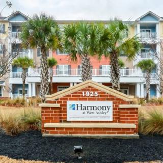 A residential complex with a Harmony at West Ashley sign and palm trees in front.