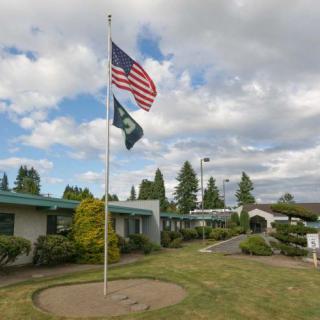 A flagpole with the USA flag and another flag in front of a building on a cloudy day.