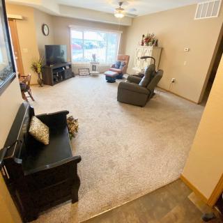 A cozy living room with comfortable seating and a television, featuring neutral tones and ample natural light from a large window.