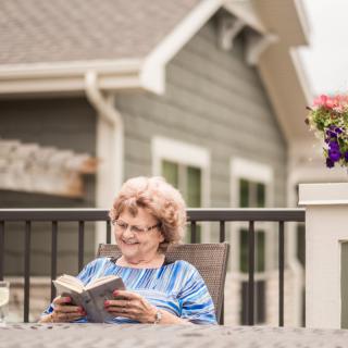 An elderly woman enjoying a book outdoors on a patio.