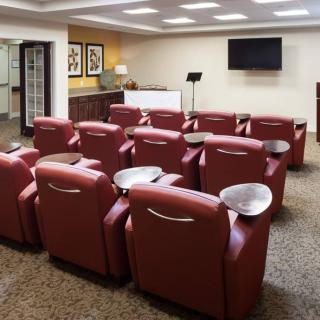 A cozy theater room with red leather recliners arranged in rows facing a large screen.