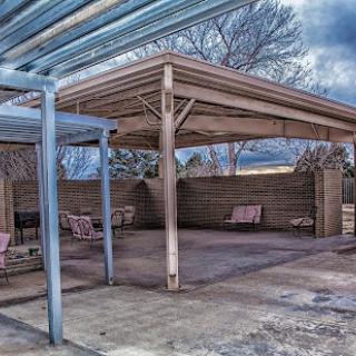 An empty outdoor patio area with a canopy and benches, set against a cloudy sky.