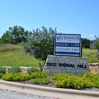 A roadside sign for a memory care and assisted living facility surrounded by landscaping.