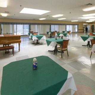 A spacious dining area with neatly arranged tables and chairs, featuring a piano in the corner.