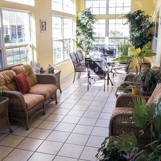 A bright sunroom with comfortable seating, abundant plants, and large windows allowing natural light.