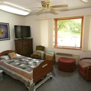 A cozy room with a hospital bed, TV, and a large window letting in natural light.