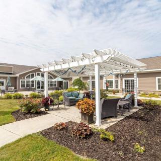 A manicured garden featuring a white pergola with outdoor seating in front of a building.