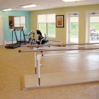 A well-equipped rehabilitation room featuring parallel bars, a treadmill, and a stationary bike.