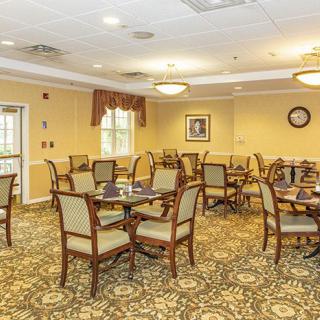 An empty dining room with neatly arranged tables and chairs, featuring warm lighting and patterned carpet.