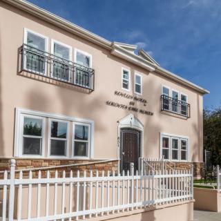 A two-story house with a light pink facade, featuring multiple windows and a white fence in the foreground.