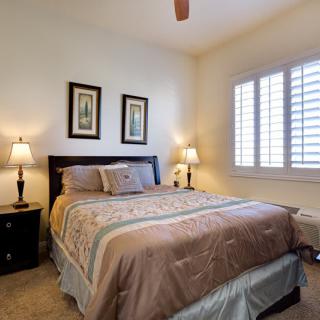 A cozy bedroom with a neatly made bed, bedside tables with lamps, and a window with shutters.