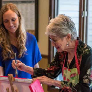 An elderly woman and a younger woman engaging in a painting activity together.