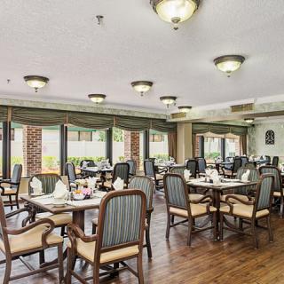 A well-lit dining area with elegantly arranged tables and chairs, featuring large windows and wooden flooring.