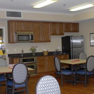A modern kitchen and dining area featuring wooden cabinets, a refrigerator, microwave, tables, and chairs.
