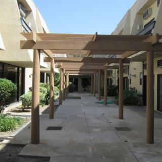 A walkway with wooden pergolas casting shadows on the ground.