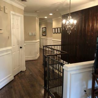 A well-lit hallway with wooden flooring, featuring a chandelier and decorative wall paneling.