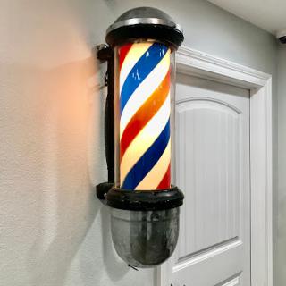 A classic barber pole with red, white, and blue stripes illuminated in a barbershop setting.