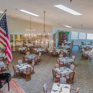 A spacious dining room featuring multiple tables set for guests, illuminated by elegant chandeliers, with an American flag displayed prominently.