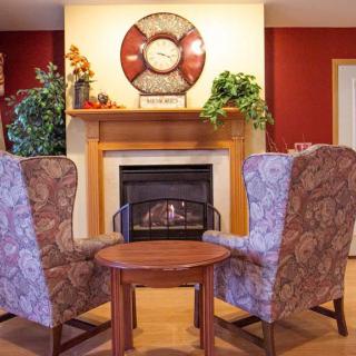 A cozy living room featuring a warm fireplace, two patterned chairs, and a small round table.