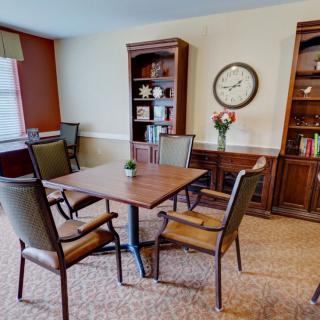 A cozy living room with a wooden table and chairs, flanked by bookshelves and adorned with a wall clock.